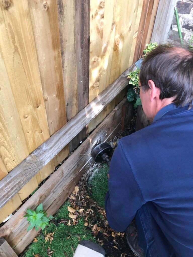 A hedgehog hole being drilled in a fence.